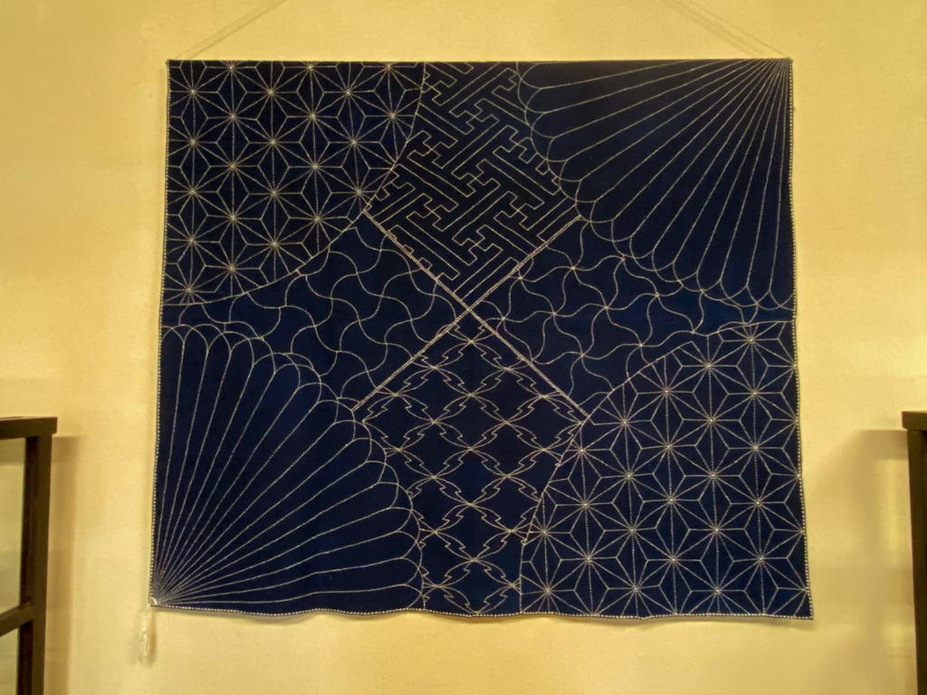 群青色の布地に生糸で刺し子の模様が施されたされた生地が壁に掛けられている。