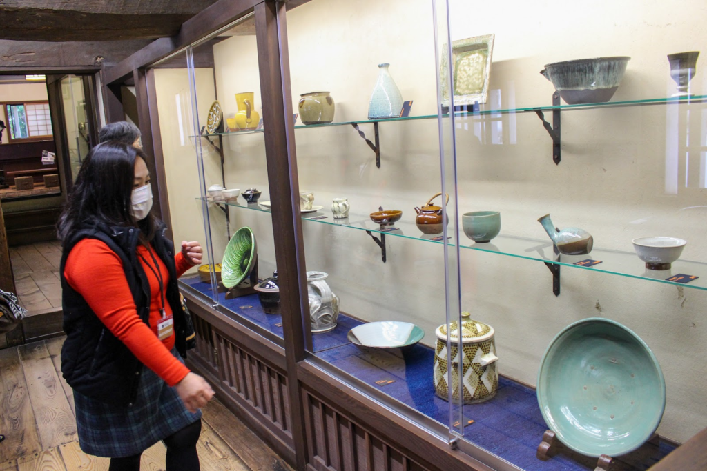 倉敷民藝館に展示される様々な色カタチの陶器とそれを眺めるツアー参加者